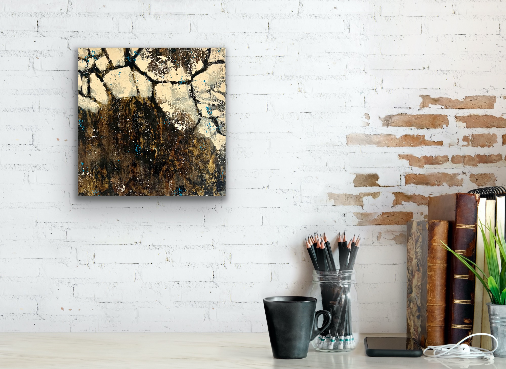 A small, square painting in black and gold in a white wall above a table