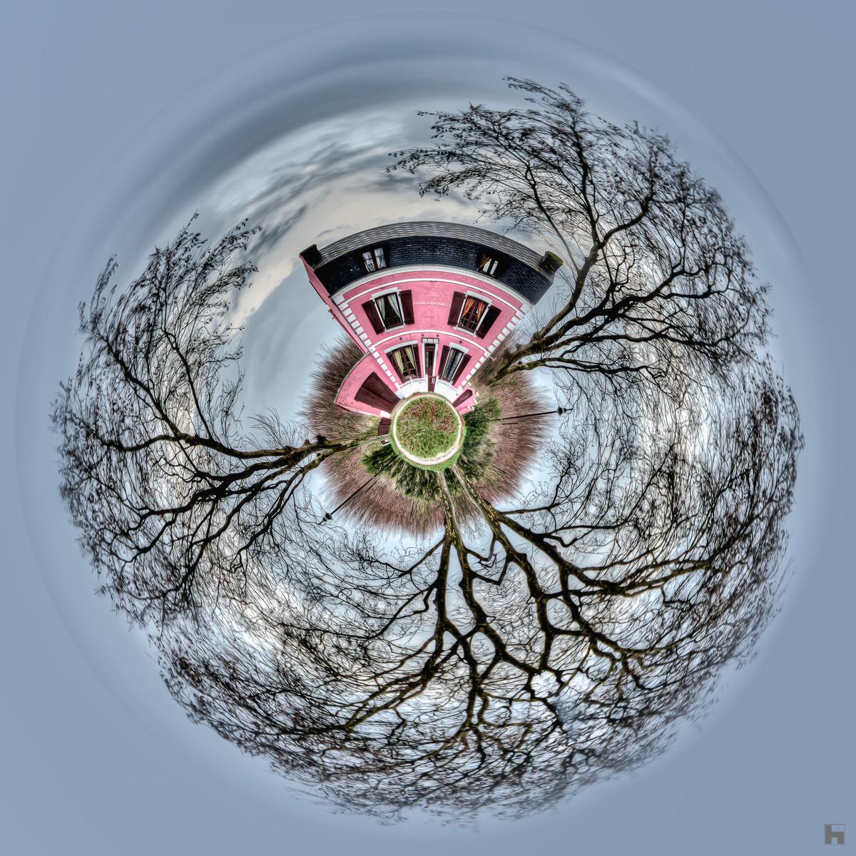 Photographie artistique "La Maison Rose" de Paul Marnef, montrant une maison rose entourée d'arbres aux branches dénudées dans un univers circulaire, issue de la série "Planètes Imaginaires", disponible en finition Chromaluxe et en édition limitée.