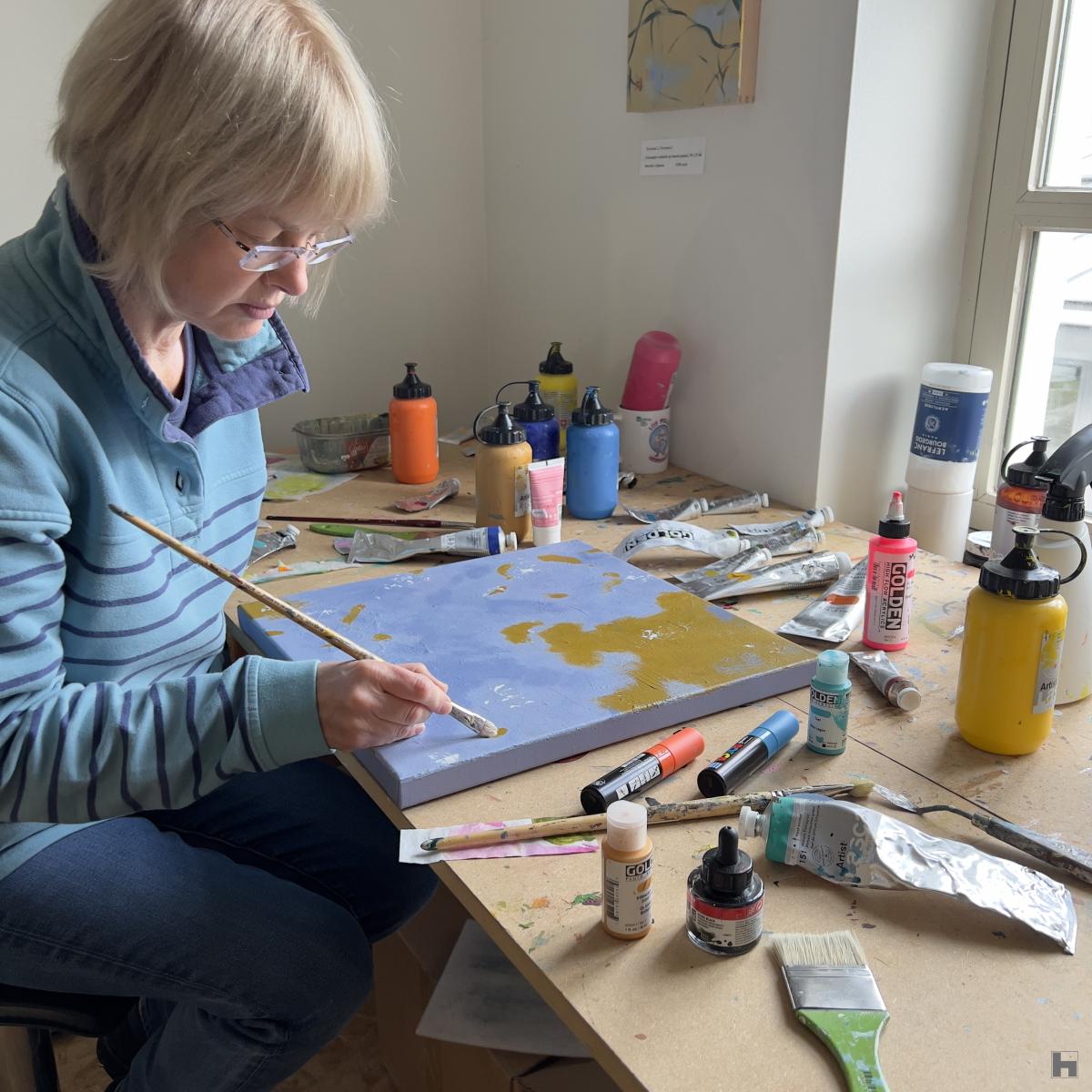 The artist sitting at her desk, working on the small, blue painting