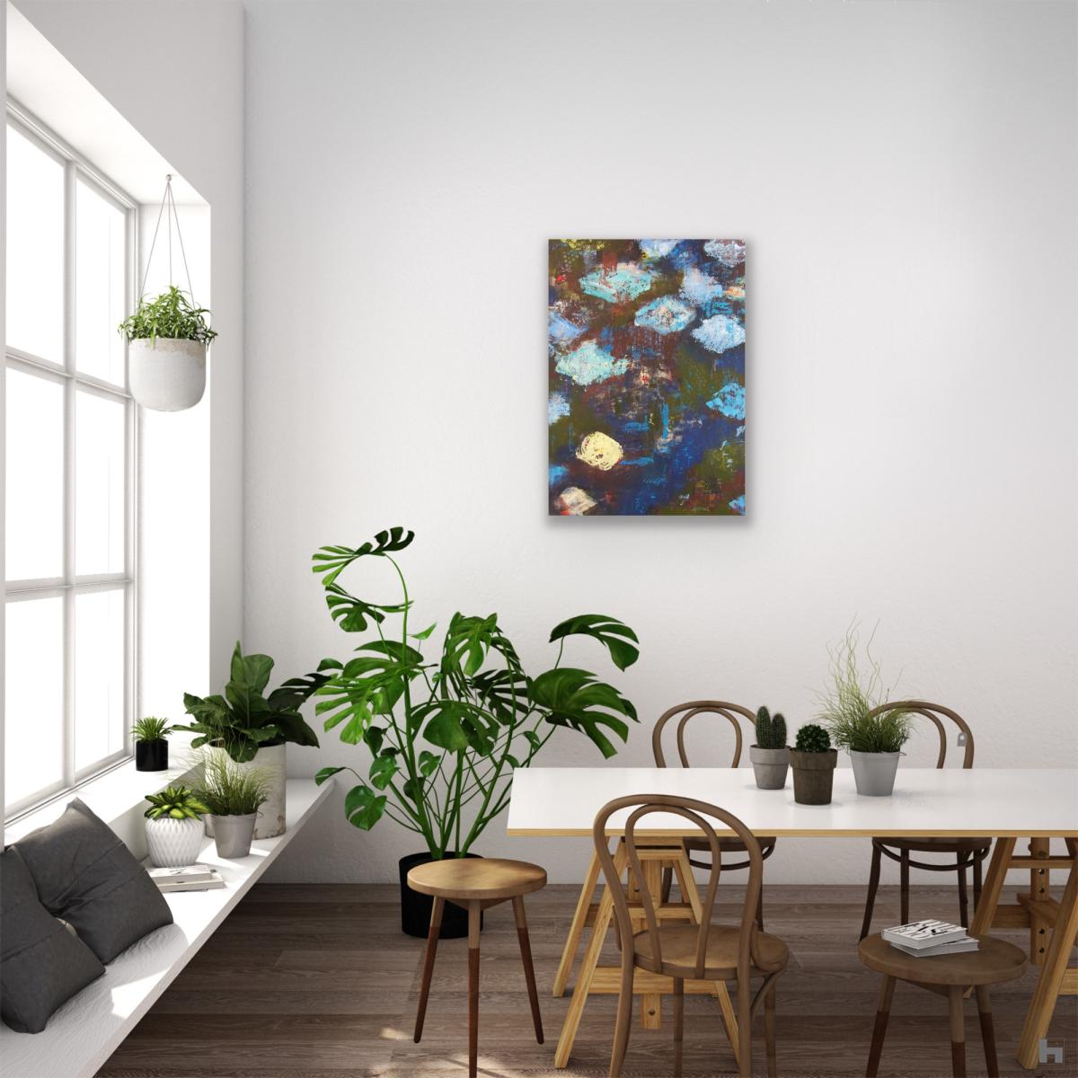A green and blue abstract painting in a room with a table and house plants