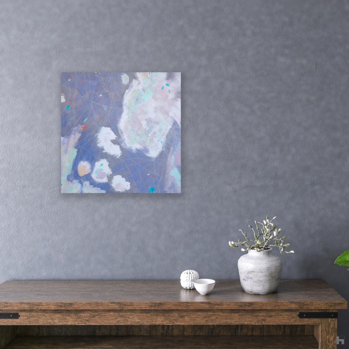 An abstract painting in soft greys hanging on a wall above a table