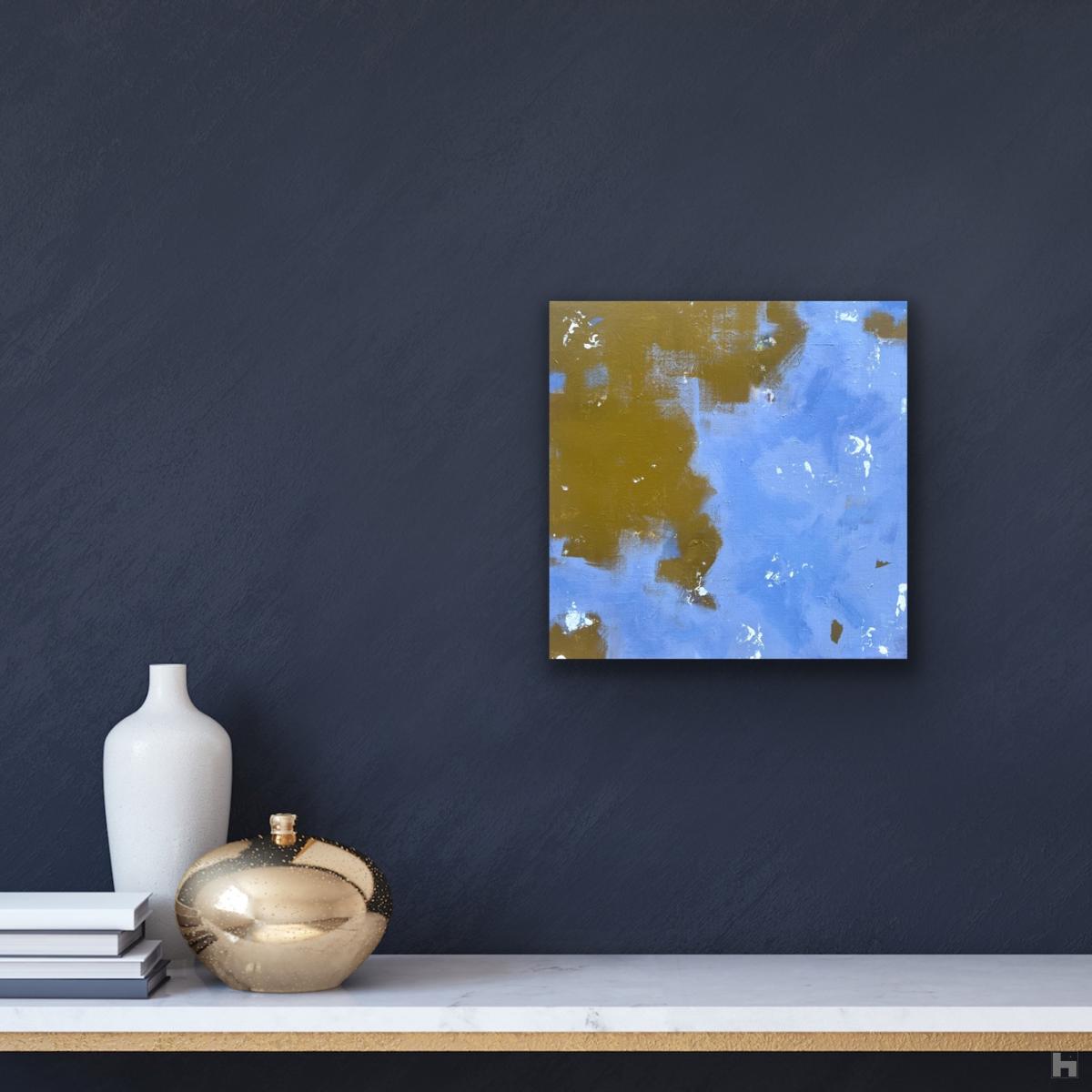 A small, square painting in blue and ochre, hanging on a dark blue wall.