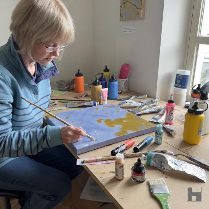 The artist sitting at her desk, working on the small, blue painting